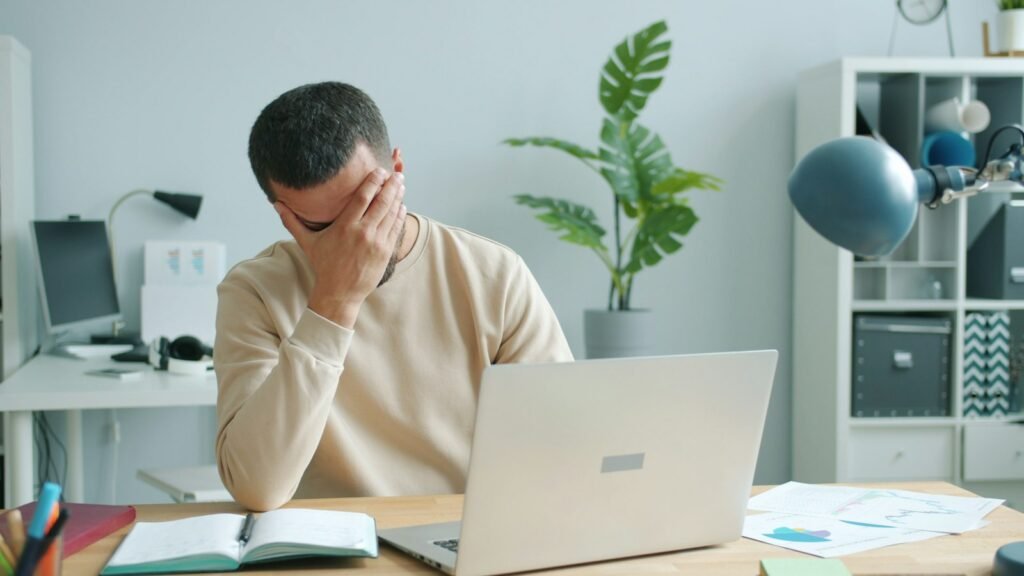 Man at a laptop rubbing his face after a long day at the desk